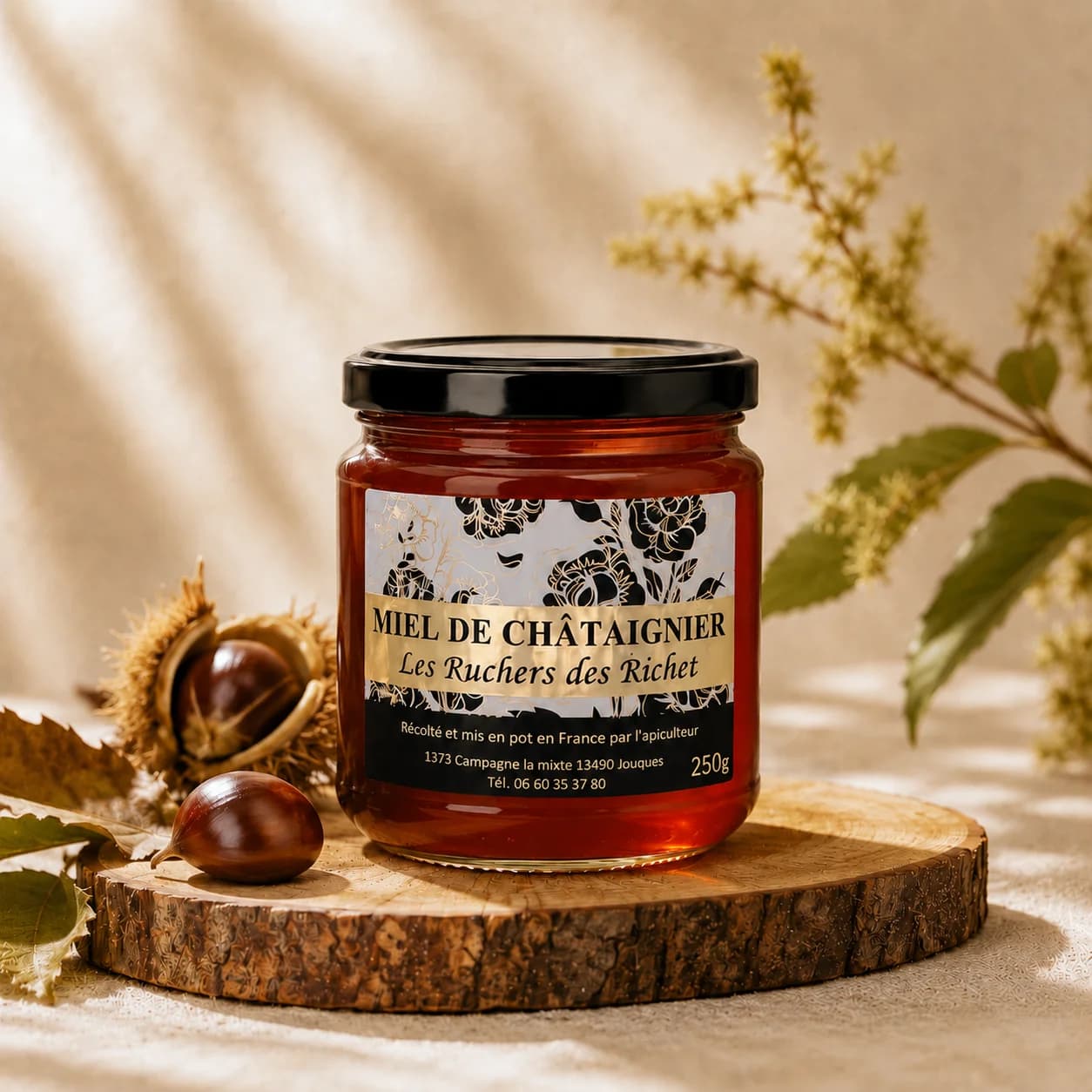 Pot de miel de châtaignier Les Ruchers des Richet fermé, posé sur une rondelle de bois, entouré de châtaignes et de feuilles de châtaignier